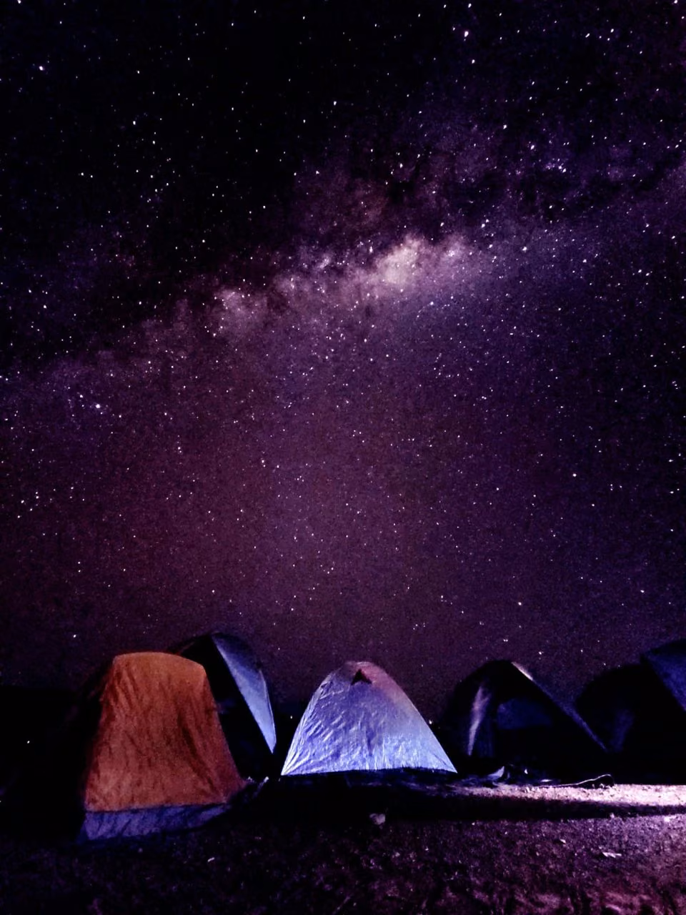 Via Láctea atravessando o céu sobre barracas iluminadas no Camping Selvagem do mirante