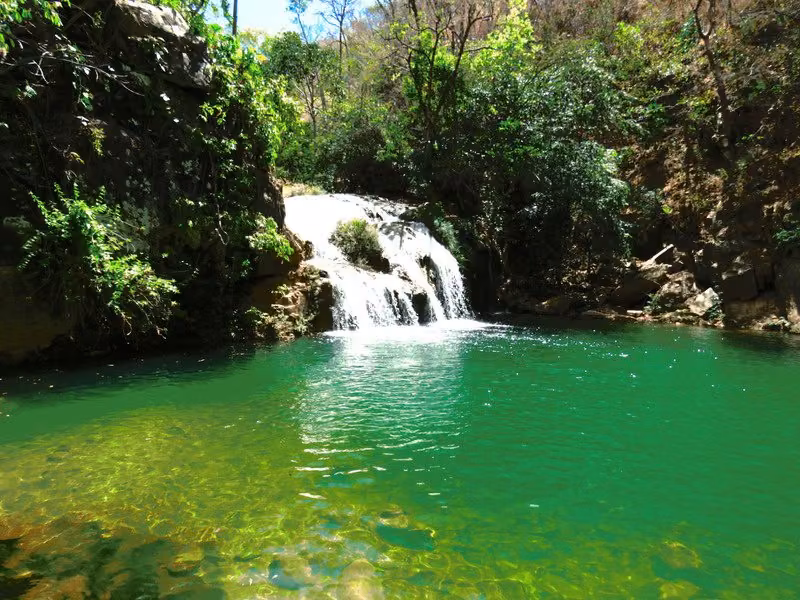 Poço Esmeralda: água verde e transparente recebendo uma pequena queda entre pedras e mata